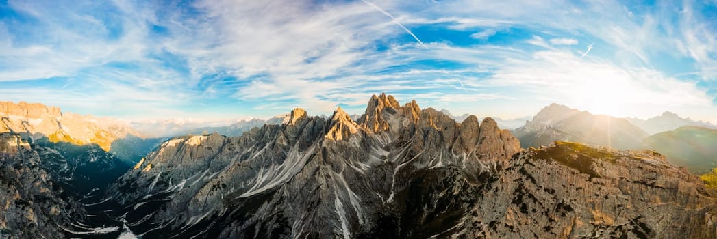 Mountain landscape at sunrise. Rising sun rays illuminate stony treeless slopes of Three Peaks of Lavaredo under clear sky aerial view in back lit