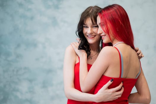 A close-up portrait of two tenderly embracing women dressed in identical red dresses. Lesbian intimacy