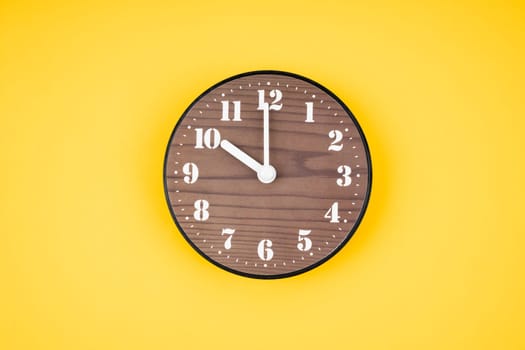 Retro wooden clock at 10 O' clock on yellow color background.