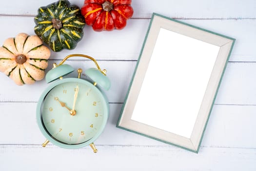 Top view of blank photo frame and vintage alarm clock with pumpkin on wooden background, Save clipping path.