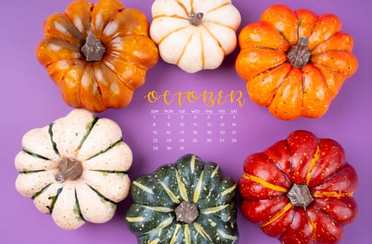 October 2023 Calendar and pumpkins on purple cardboard background.