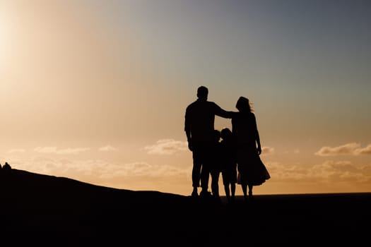 Parents, kids and silhouette on mountain, sunset and hug with love, care and summer adventure. Mother, father and young children with sky background, space and outdoor on holiday, vacation or journey.