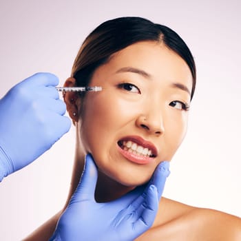 Face injection, skincare and Asian woman in pain in studio isolated on a white background. Cosmetics, syringe and female model with collagen filler, dermatology and prp facelift in plastic surgery