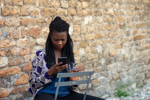 Close up portrait of beautiful young african american woman reading answering text message on mobile phone app over a wall outdoors