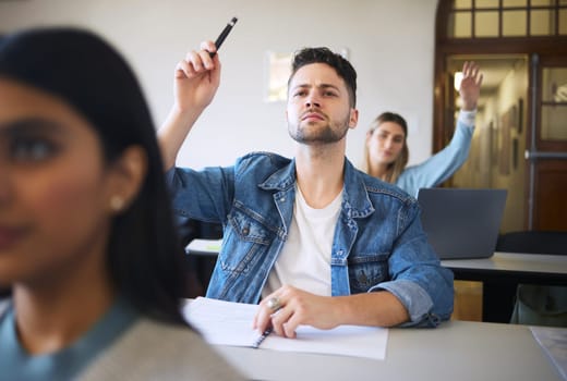 Students question, hand raise and classroom for learning, education or college with notebook on desk. College student group, university class or lecture for knowledge, development or focus for future.