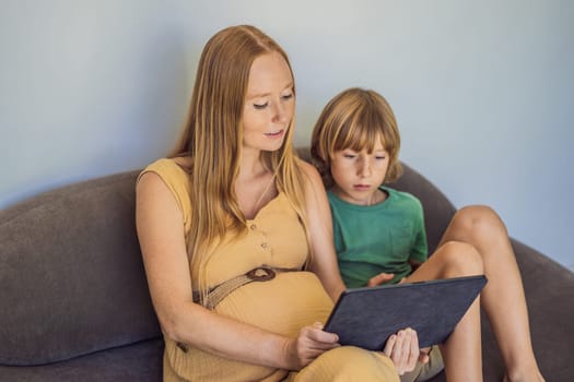 pregnant mom and son look at the tablet. Reading a book or watching a cartoon or making a video call. Look at the photo from the ultrasound.