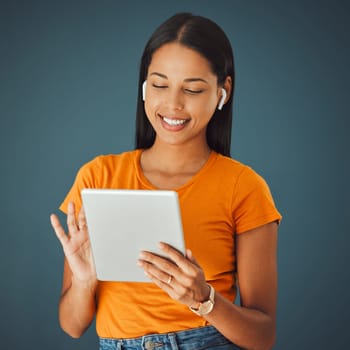 Woman, tablet and listening to music online while streaming and happy on a studio background. Smile of a young gen z person with mobile app for podcast, radio or audio with network internet to relax.