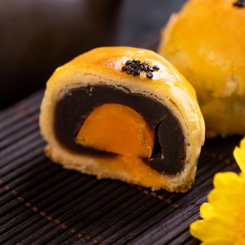 Tasty baked egg yolk pastry moon cake for Mid-Autumn Festival on black slate dark background. Chinese festive food concept, close up, copy space.