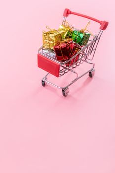 Annual sale, Christmas shopping season concept - mini red shop cart trolley full of gift box isolated on pale pink background, copy space, close up