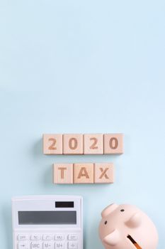 2020 goal, finance plan abstract design concept, wood blocks on blue table background with piggy bank and calculator, top view, flat lay, copy space.