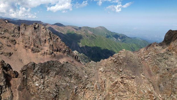 Stone peaks with cliffs. Grass grows in places. There is white snow on the glacier. There are signs made of stones and tablets. A mountainous area with large stones. Bogdanovich Glacier, Kazakhstan