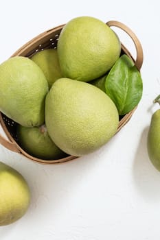 Fresh pomelo, pummelo, grapefruit, shaddock on white cement background in bamboo basket. Autumn seasonal fruit, top view, flat lay, tabletop shot.