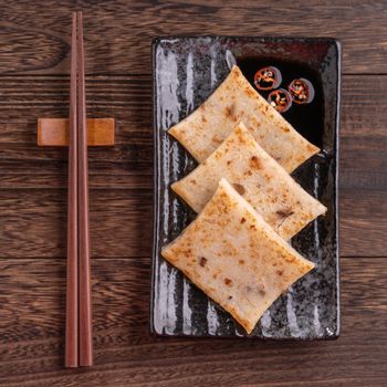 Delicious turnip cake, Chinese traditional local radish cake in restaurant with soy sauce and chopsticks, close up, copy space, top view, flat lay.