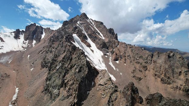 High rocky mountains are sometimes covered with ice and snow. A huge glacier passes between the peaks. The ice is gradually melting. The stones are lying on glacier. Steep cliffs. The view from drone