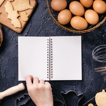 Woman is reading cookbook recipe of making Halloween cookies with baking ingredients, design concept of cooking class, top view, flat lay, overhead.