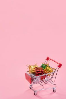 Annual sale, Christmas shopping season concept - mini red shop cart trolley full of gift box isolated on pale pink background, copy space, close up