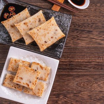 Delicious turnip cake, Chinese traditional local radish cake in restaurant with soy sauce and chopsticks, close up, copy space, top view, flat lay.