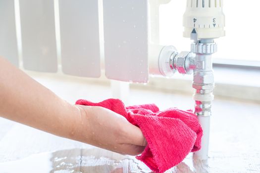 Female hand with rag cleaning water from heating radiator