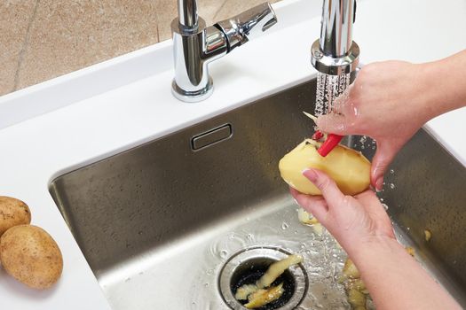 Cropped view of female hands peeling potato over Food waste disposer machine
