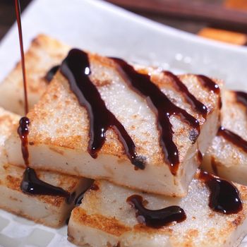 Pouring black soy sauce on ready-to-eat delicious turnip cake, Chinese traditional local dish radish cake in restaurant, close up, copy space.