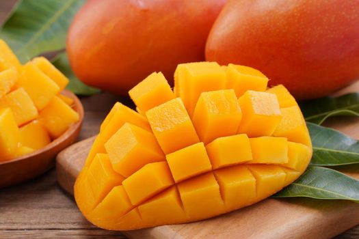 Fresh mango, beautiful chopped fruit with green leaves on dark wooden table background. Tropical fruit design concept. Flat lay. Top view. Copy space