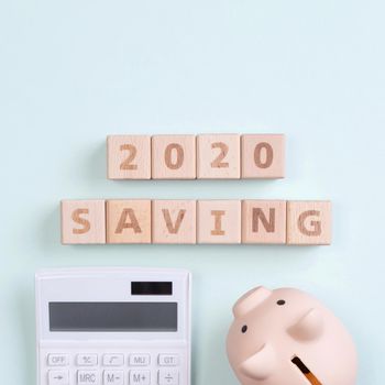 2020 goal, finance plan abstract design concept, wood blocks on green table background with piggy bank and calculator, top view, flat lay, copy space.