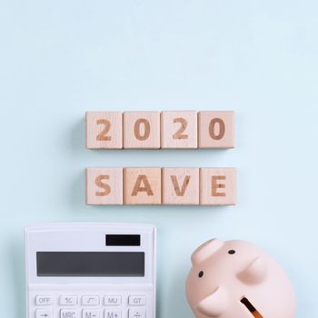 2020 goal, finance plan abstract design concept, wood blocks on green table background with piggy bank and calculator, top view, flat lay, copy space.