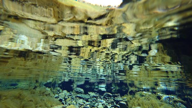 An incredible underwater world of a mountain river. Crystal clear clear water. Yellow rocks and green-brown algae. The rays of light are refracted into a blue color in the distance. An unusual world