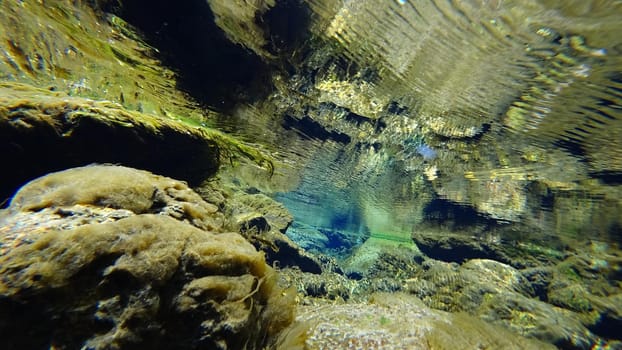 An incredible underwater world of a mountain river. Crystal clear clear water. Yellow rocks and green-brown algae. The rays of light are refracted into a blue color in the distance. An unusual world