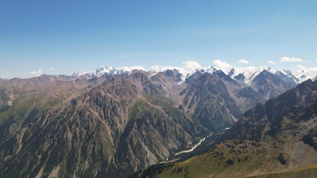 High mountains covered with snow in places. Green grass grows. Huge rocks and cliffs. In the distance, you can see peak of Talgar and Nursultan. A rocky gorge. Rowing peaks from a height. Kazakhstan