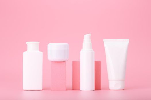 Trendy composition in pink colors with set of cosmetic bottles with beauty products on geometric props against bright pink background. Concept of anti acne or regular basic skin treatment