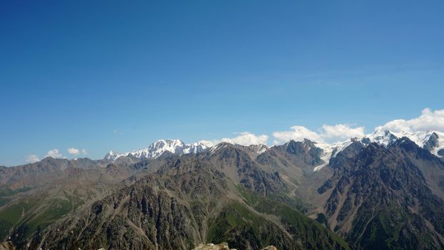 High mountains covered with snow in places. Green grass grows. Huge rocks and cliffs. In the distance, you can see peak of Talgar and Nursultan. A rocky gorge. Rowing peaks from a height. Kazakhstan