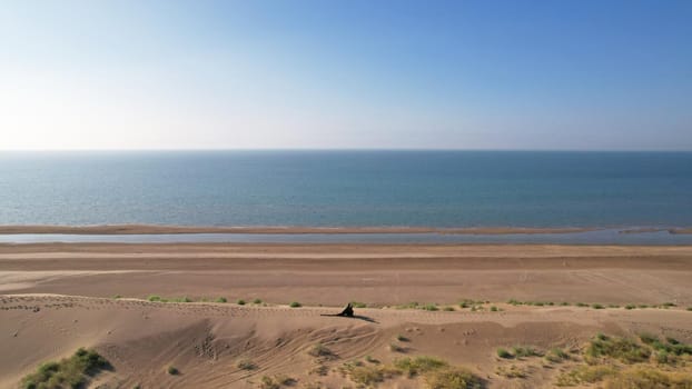 A young couple walk along a sand dune near the sea. Top view. A shadow falls on the sand from the sun. A long train of the dress. They are dressed in black. Lovers ' walk. The blue water of the sea