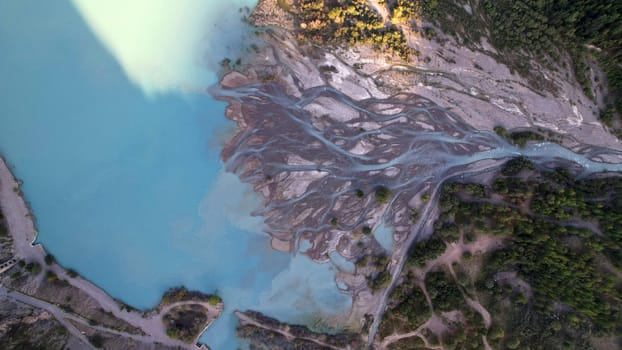 View of the mountain lake Issyk from a height. Turquoise-emerald water from the glacier. Reflection of mountains, forests and the sun on the water. The river flows into the lake. Issyk Dam. Kazakhstan