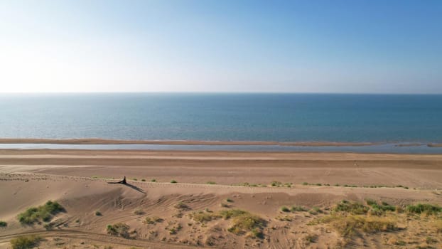 A young couple walk along a sand dune near the sea. Top view. A shadow falls on the sand from the sun. A long train of the dress. They are dressed in black. Lovers ' walk. The blue water of the sea