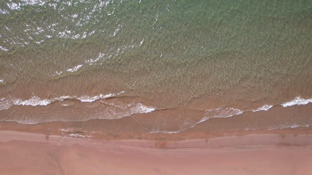 The sea touches the yellow sand with waves. Top view from a drone on a clean beach and emerald water. The sun's rays are reflected in the water. Clear blue sky. A place for relaxation. Kapchagai