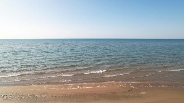 The sea touches the yellow sand with waves. Top view from a drone on a clean beach and emerald water. The sun's rays are reflected in the water. Clear blue sky. A place for relaxation. Kapchagai