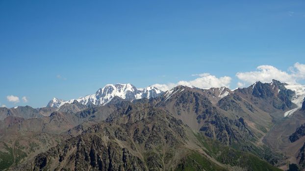 High mountains covered with snow in places. Green grass grows. Huge rocks and cliffs. In the distance, you can see peak of Talgar and Nursultan. A rocky gorge. Rowing peaks from a height. Kazakhstan