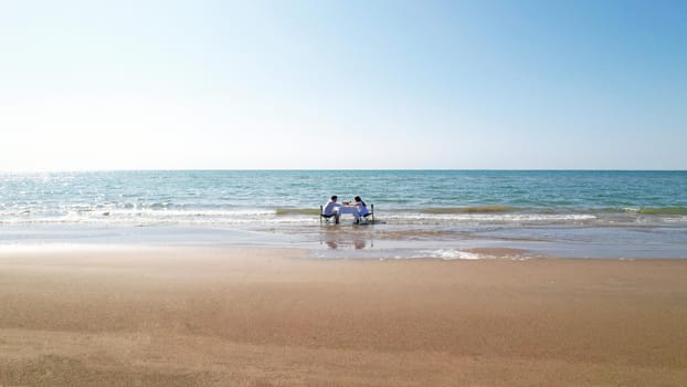 A couple in love at a table on the beach. They enjoy breakfast and the beauty of nature. Turquoise water, yellow sand and blue sky. A romantic dinner. Top view from the drone. Kapchagai, Kazakhstan.