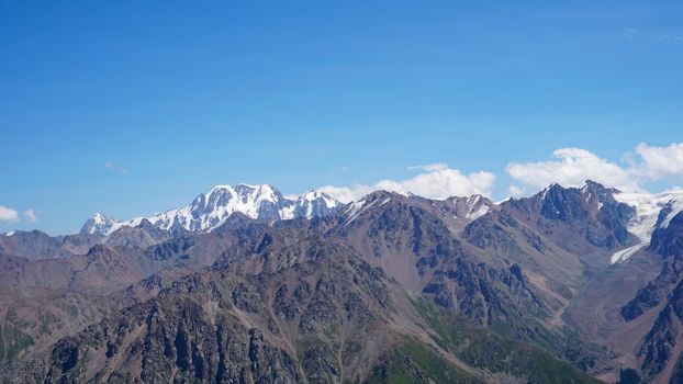 High mountains covered with snow in places. Green grass grows. Huge rocks and cliffs. In the distance, you can see peak of Talgar and Nursultan. A rocky gorge. Rowing peaks from a height. Kazakhstan