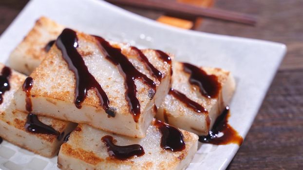 Pouring black soy sauce on ready-to-eat delicious turnip cake, Chinese traditional local dish radish cake in restaurant, close up, copy space.