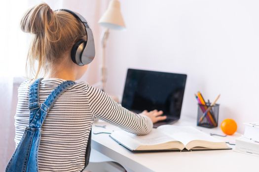 Little girl doing her homework at home and using a laptop