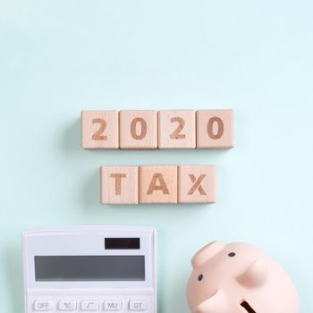 2020 goal, finance plan abstract design concept, wood blocks on green table background with piggy bank and calculator, top view, flat lay, copy space.