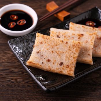 Delicious turnip cake, Chinese traditional local dish radish cake in restaurant with soy sauce and chopsticks, close up, copy space.