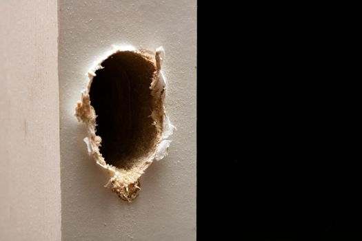 Drilled hole in a white wooden door close up
