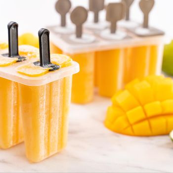Fresh mango fruit popsicle ice in the plastic shaping box on bright marble table. Summer mood concept product design, close up.