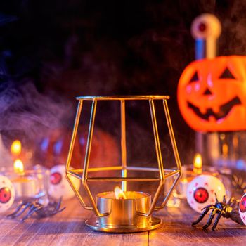 Halloween concept, orange pumpkin lantern and candles on a dark wooden table with green-orange smoke around the background, trick or treat, close up