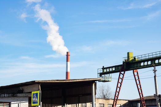 Rail gantry container crane and Industrial chimney with smoke on blue sky background