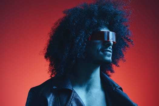 Portrait of fashion man with curly hair on red background with stylish glasses, multicultural, colored light, black leather jacket trend, modern concept. High quality photo