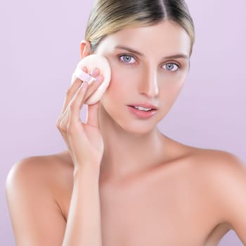 Alluring beautiful female model applying powder puff for facial makeup concept. Portrait of flawless perfect cosmetic skin woman put powder foundation on her face in pink isolated background.